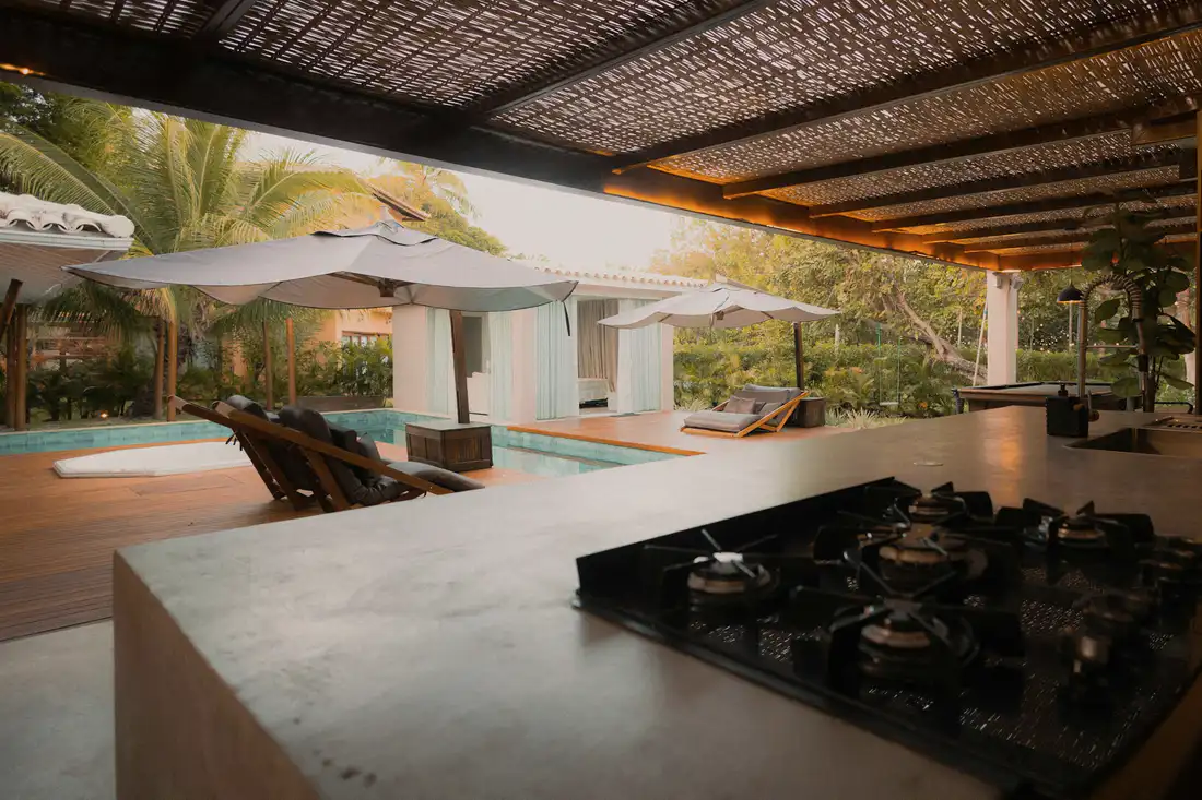Outdoor kitchen counter under a slatted roof with a pool beyond