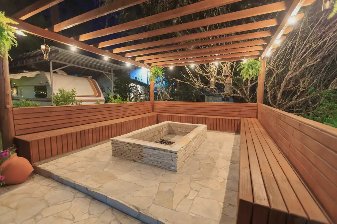 Benches and a stone fire pit under a lit pergola